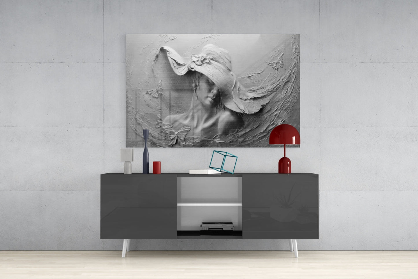 Monochromatic relief glass wall art depicting a woman's profile with flowing fabric, displayed above a dark console table with white legs and red decorative accessories.