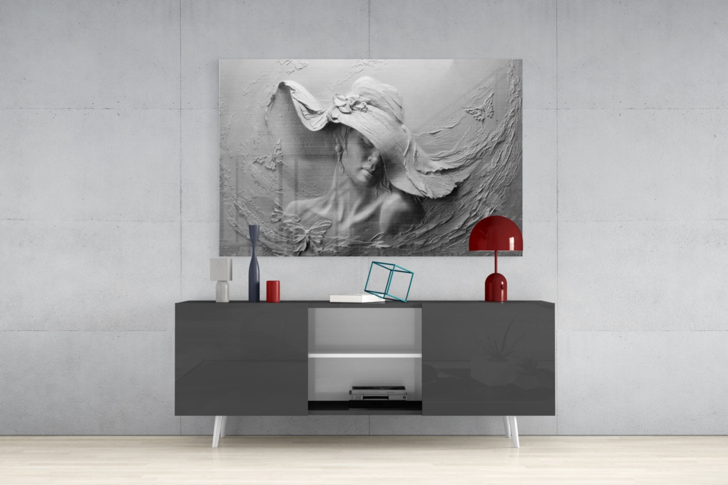 Monochromatic relief glass wall art depicting a woman's profile with flowing fabric, displayed above a dark console table with white legs and red decorative accessories.