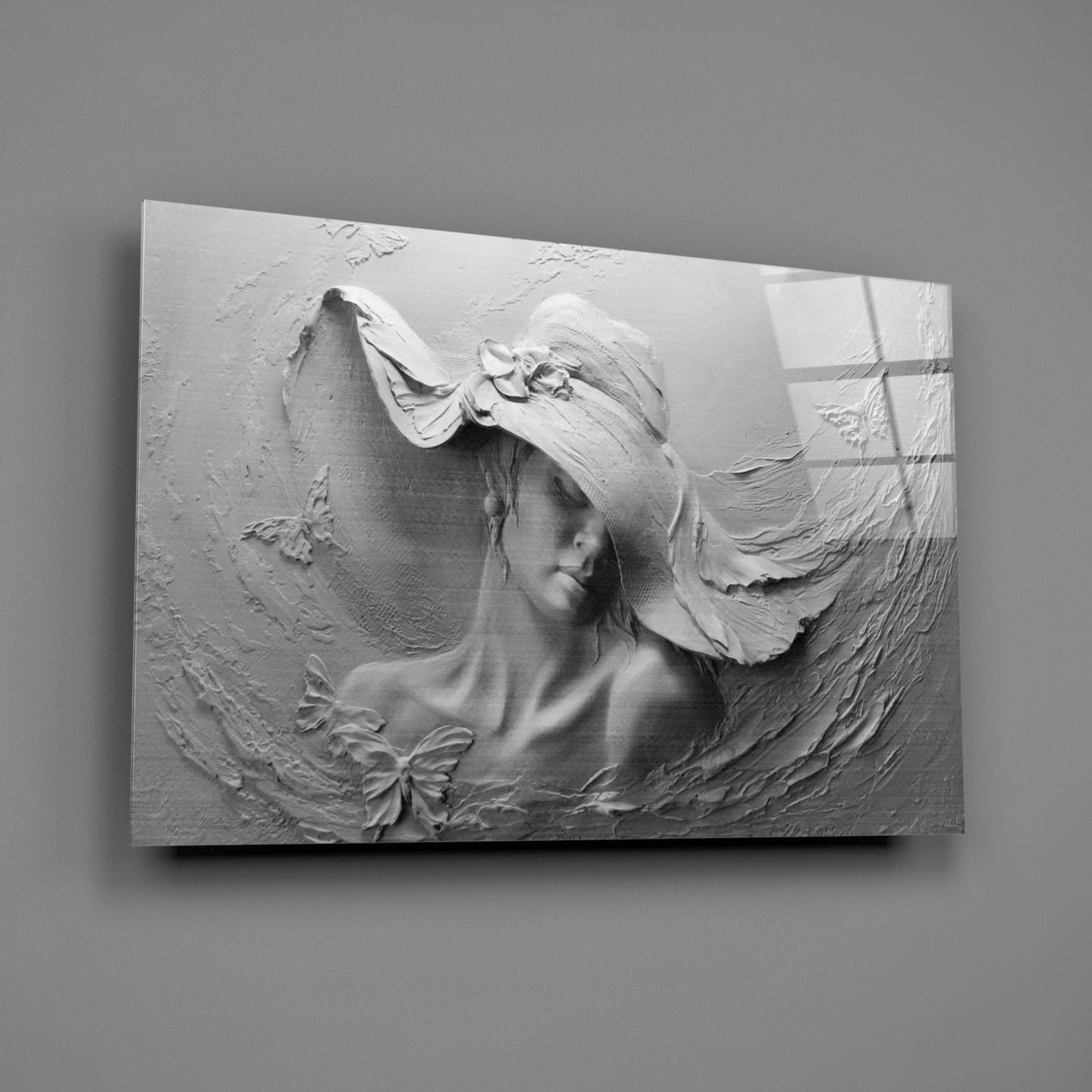 White relief sculpture on glass panel depicting a woman's profile with flowing hair and decorative bow, mounted on gray wall.