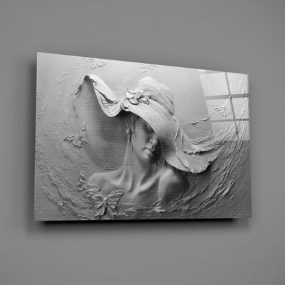 White relief sculpture on glass panel depicting a woman's profile with flowing hair and decorative bow, mounted on gray wall.