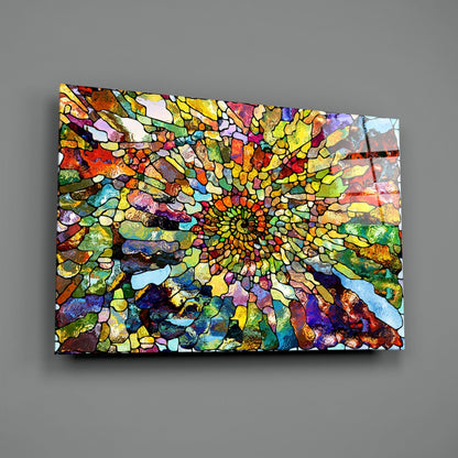 Angled perspective of colorful mosaic glass art with radiating stained glass pattern in vibrant yellows, reds, blues, and greens against gray wall.