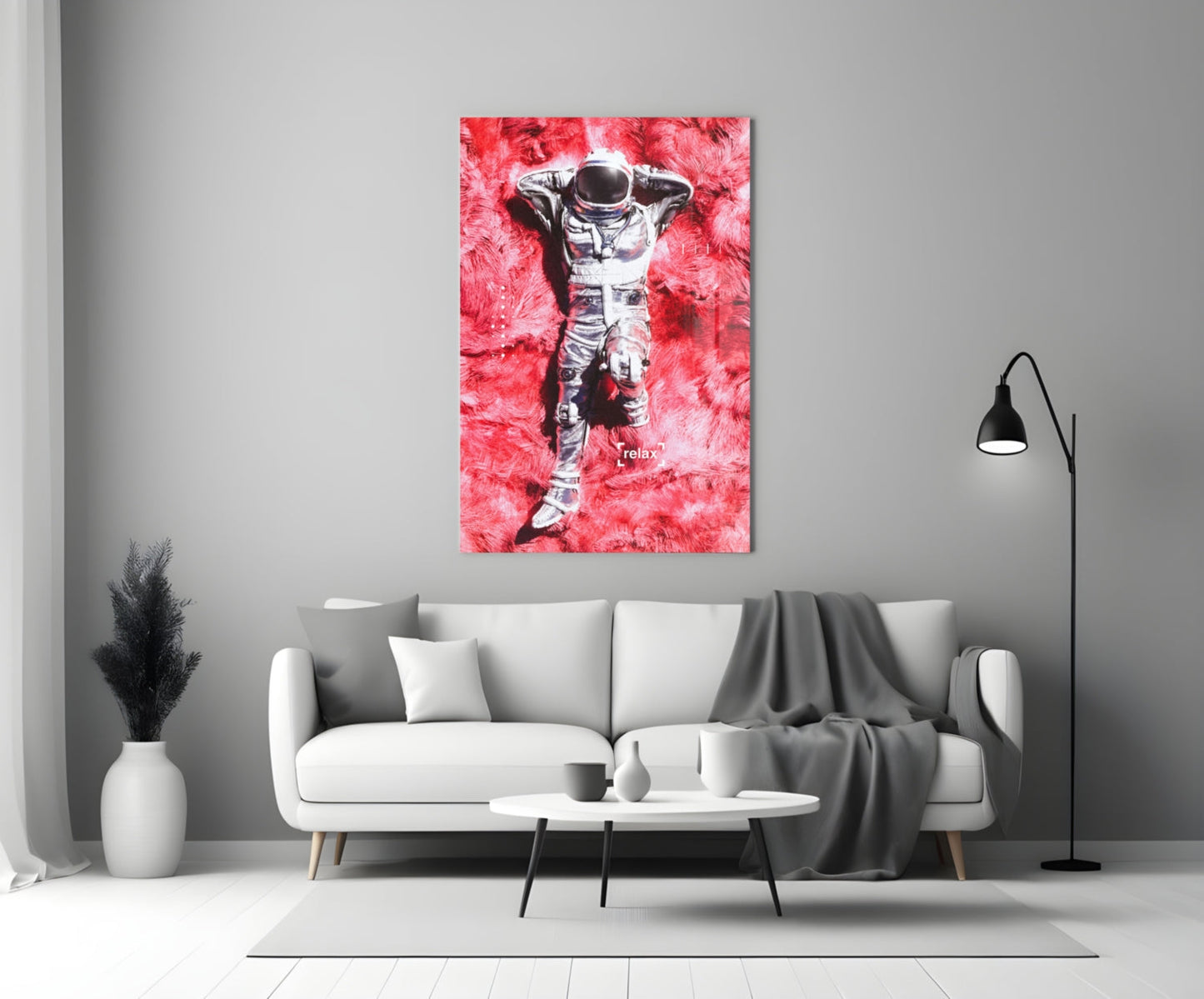 Glass art print of astronaut lying on pink textured background with "relax" text, displayed above white sofa in modern living room.
