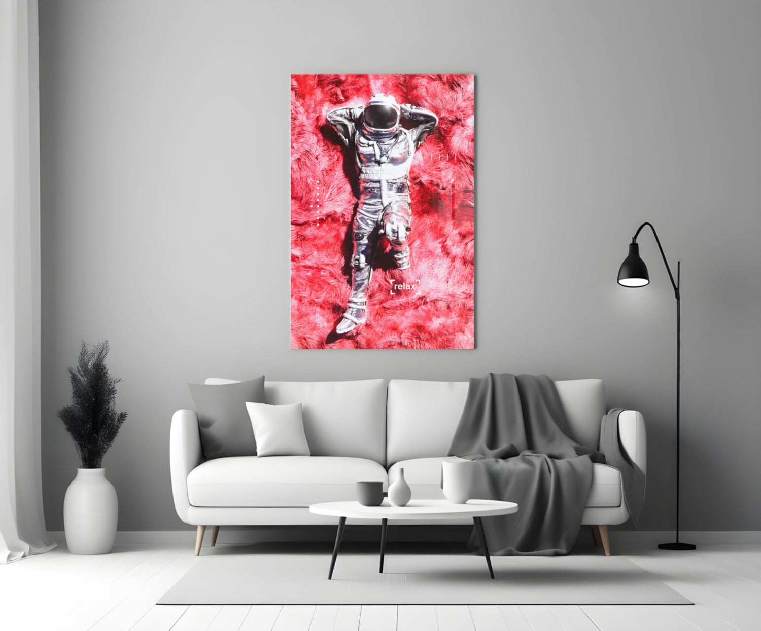 Glass art print of astronaut lying on pink textured background with "relax" text, displayed above white sofa in modern living room.