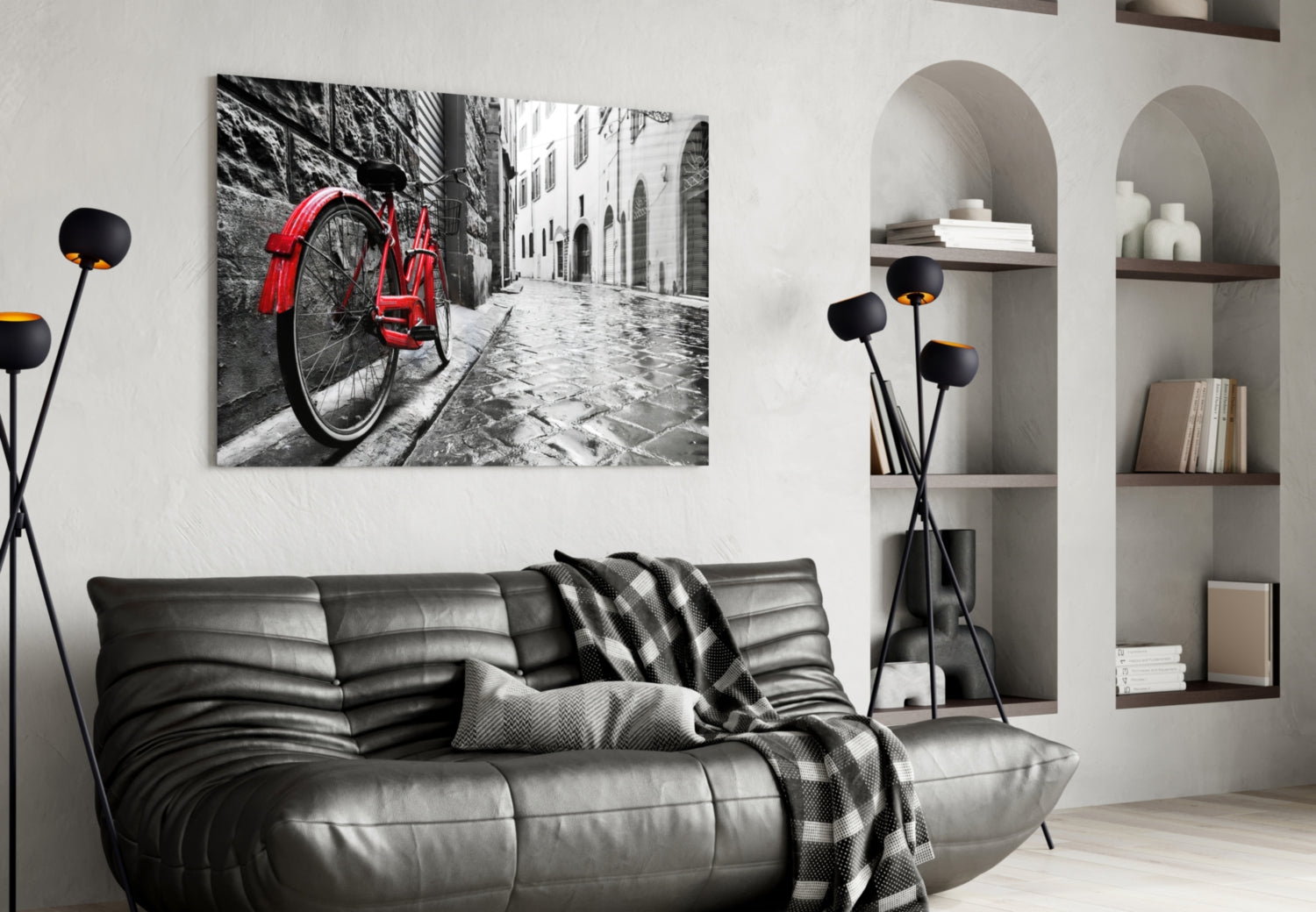Red bicycle leaning against stone wall in European cobblestone street, displayed as framed canvas art above black leather sofa.