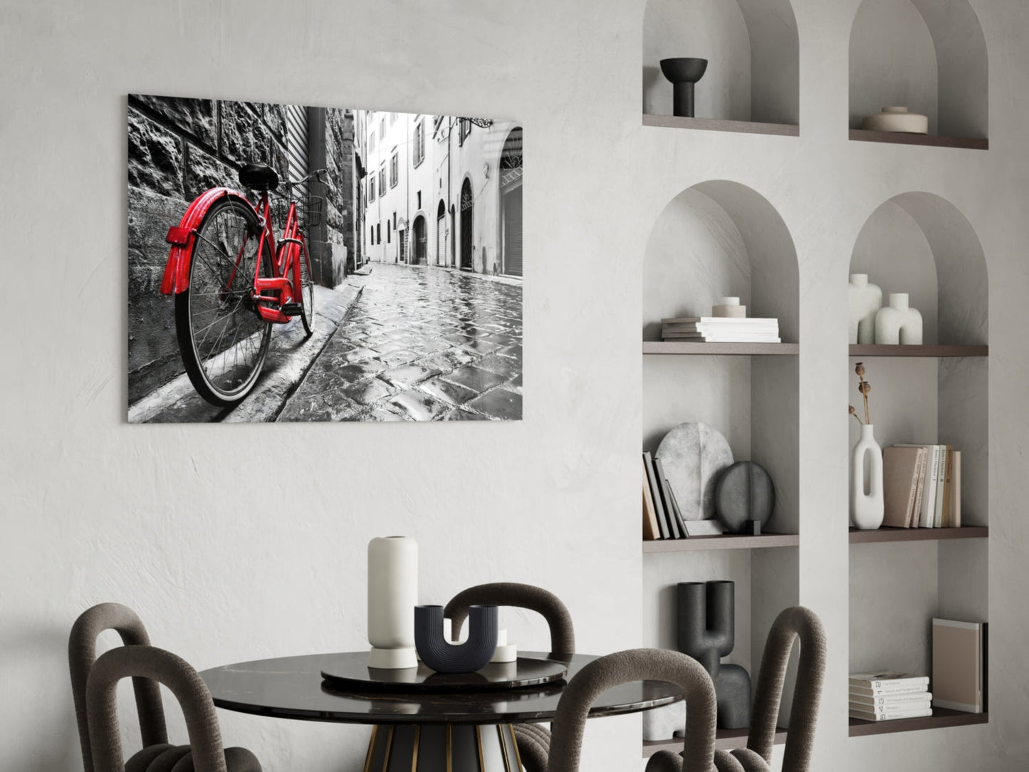 Red bicycle leaning against cobblestone European street in black and white photograph displayed on white wall.