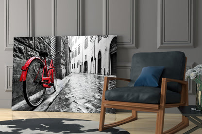 Red bicycle leaning against stone wall in black and white European street scene displayed as glass art panel in modern living room.