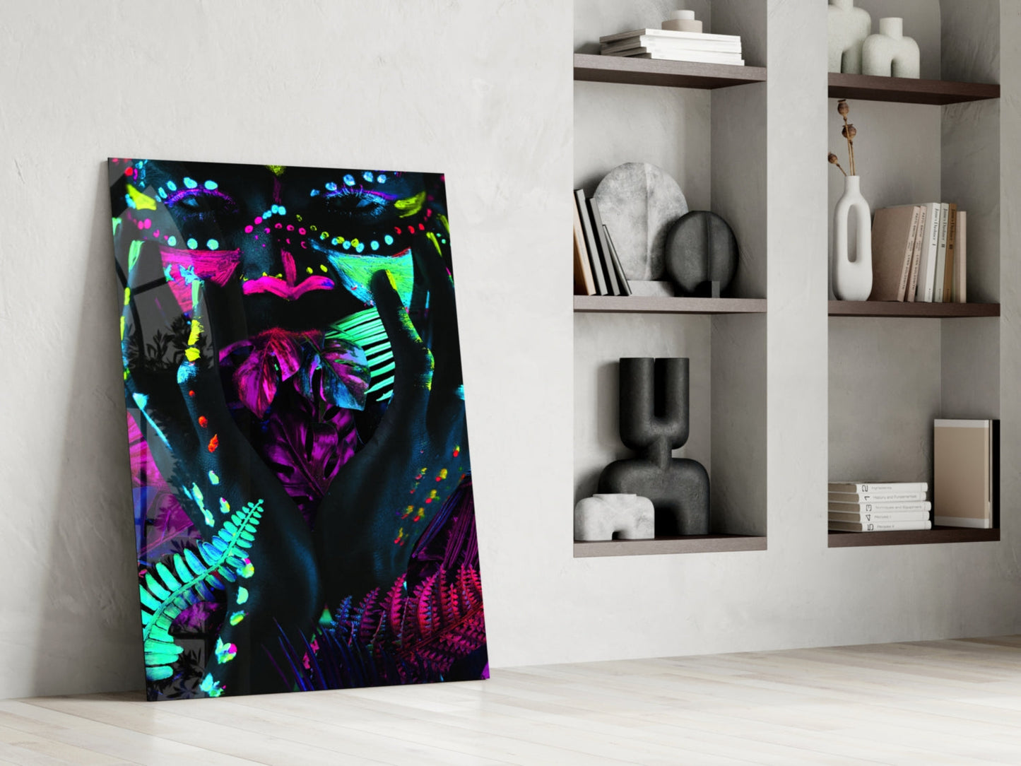 Neon Glances Glass Art leaning against white wall beside shelving, displaying vibrant neon pink, cyan, and yellow abstract face design on black background.