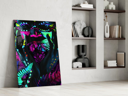 Neon Glances Glass Art leaning against white wall beside shelving, displaying vibrant neon pink, cyan, and yellow abstract face design on black background.