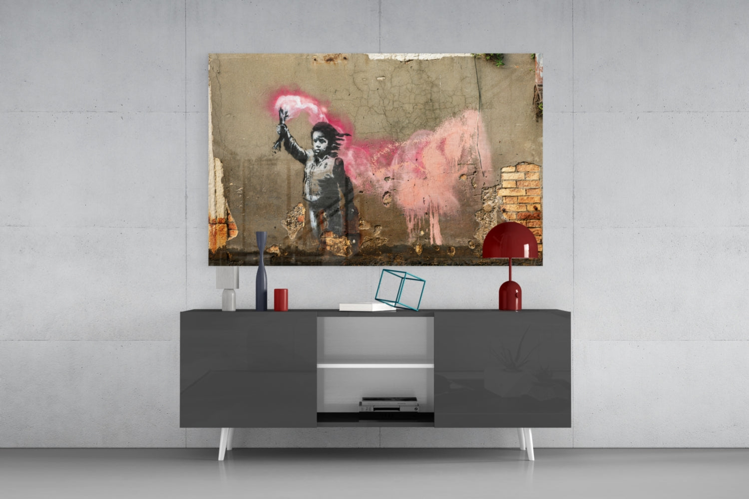 Glass art print of stenciled child holding pink spray paint displayed above modern dark media console in contemporary living room setting.
