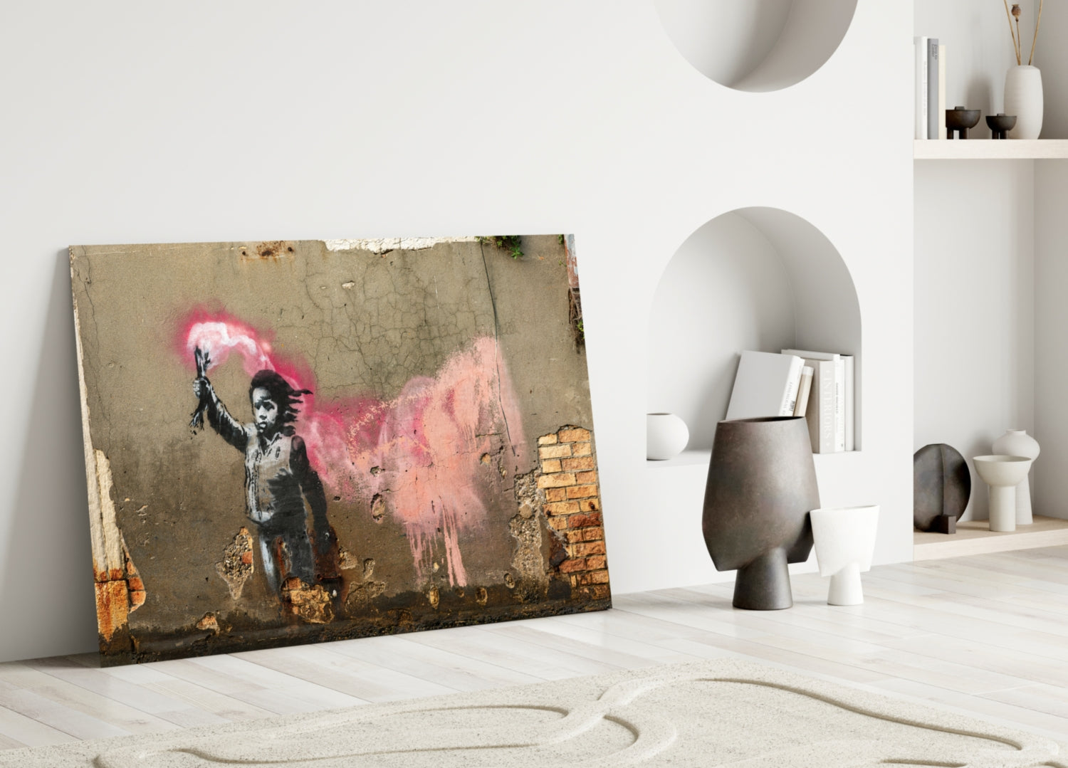 Banksy-style glass art leaning against white wall in minimalist room with pink spray-painted child figure and exposed brick detail.