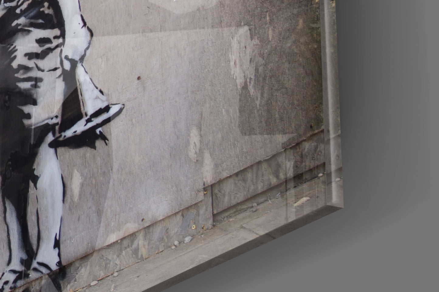 Stenciled black and white portrait on weathered concrete wall with gray pavement below, angled perspective view.