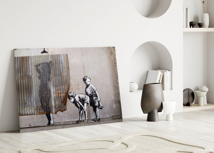Banksy-style street art glass panel leaning against white wall in minimalist interior with sand and decorative objects.