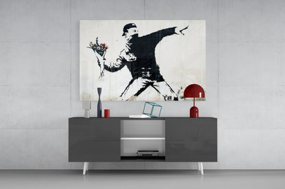 Modern living room display featuring a black and white Banksy-style stenciled artwork of a figure throwing flowers, mounted above a dark gray media console with red decorative objects.