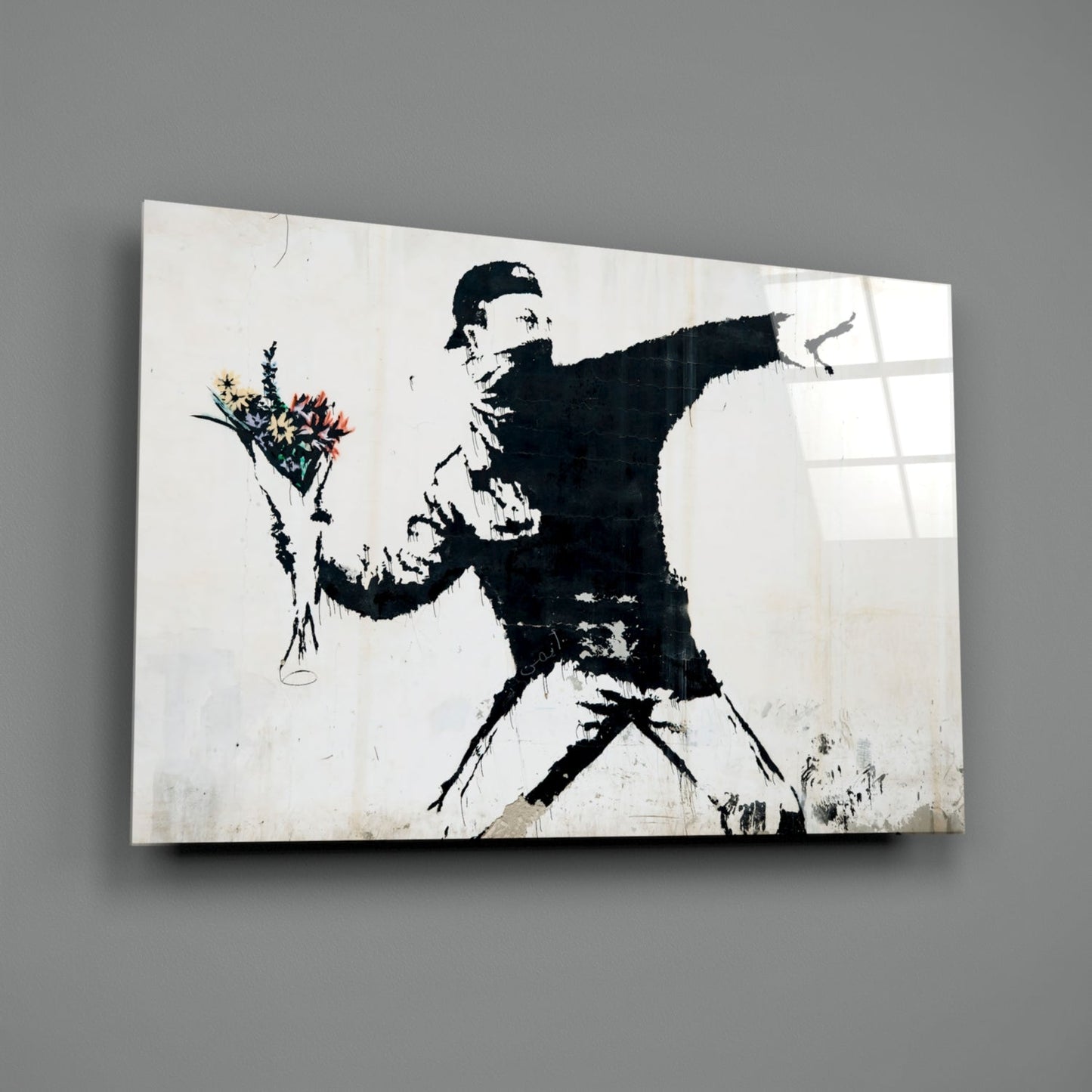 Black and white stenciled figure throwing colorful flowers on white glass panel against gray wall.
