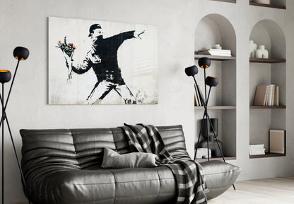Modern living room with black leather sofa displaying stenciled street art canvas of figure throwing flowers above it.