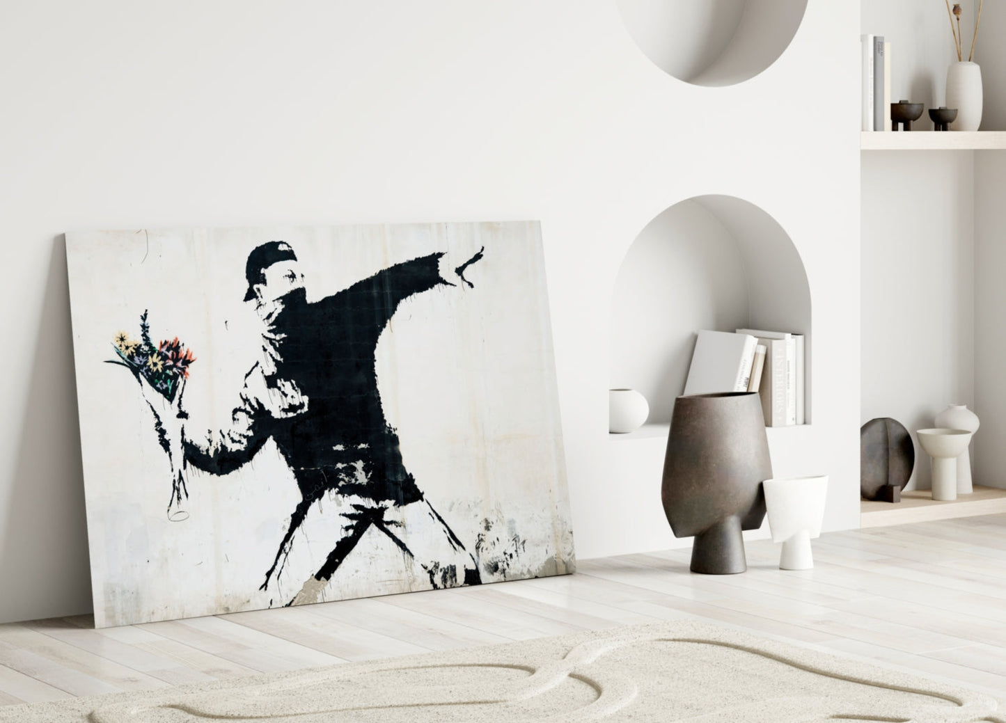 Black and white stenciled artwork of figure throwing flowers leans against white wall in minimalist interior setting.
