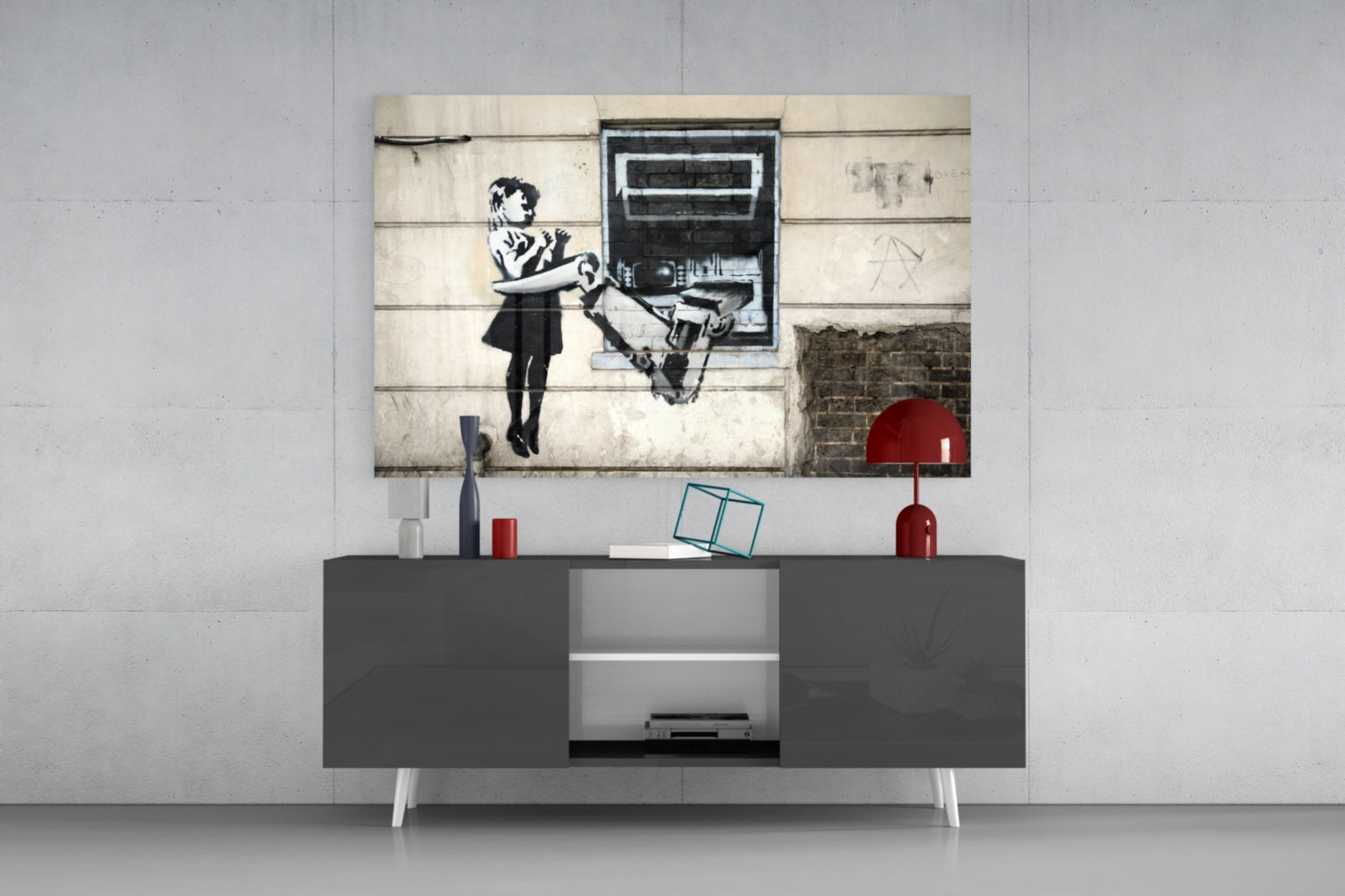 Glass art canvas mounted above gray media console displaying Banksy-style stenciled girl with robot, red accents and decorative objects visible.