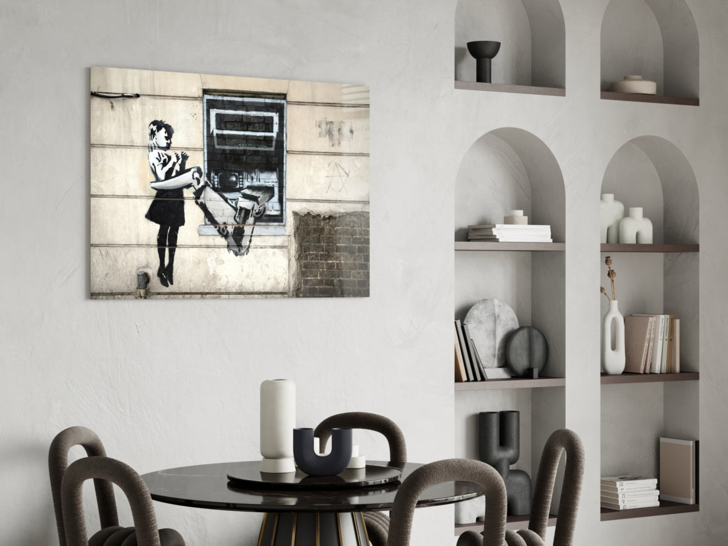 Banksy-style street art canvas displayed above black round dining table with gray upholstered chairs and white arched shelving unit.
