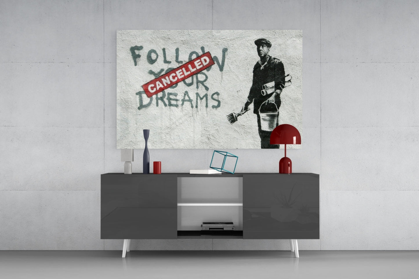 Glass art print featuring stenciled figure with "Follow Your Dreams" crossed out by red "Cancelled" banner, displayed above modern dark console table.