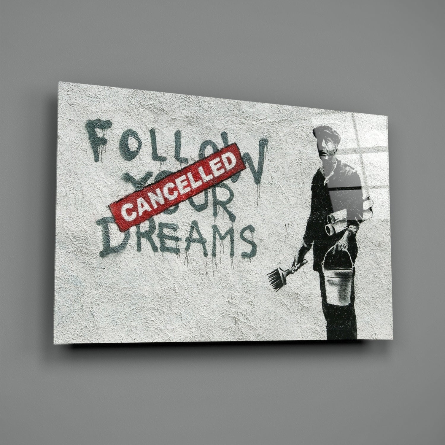 Glass art print with stenciled figure holding broom and bucket beside red "CANCELLED" stamp overlaying green text "FOLLOW YOUR DREAMS.