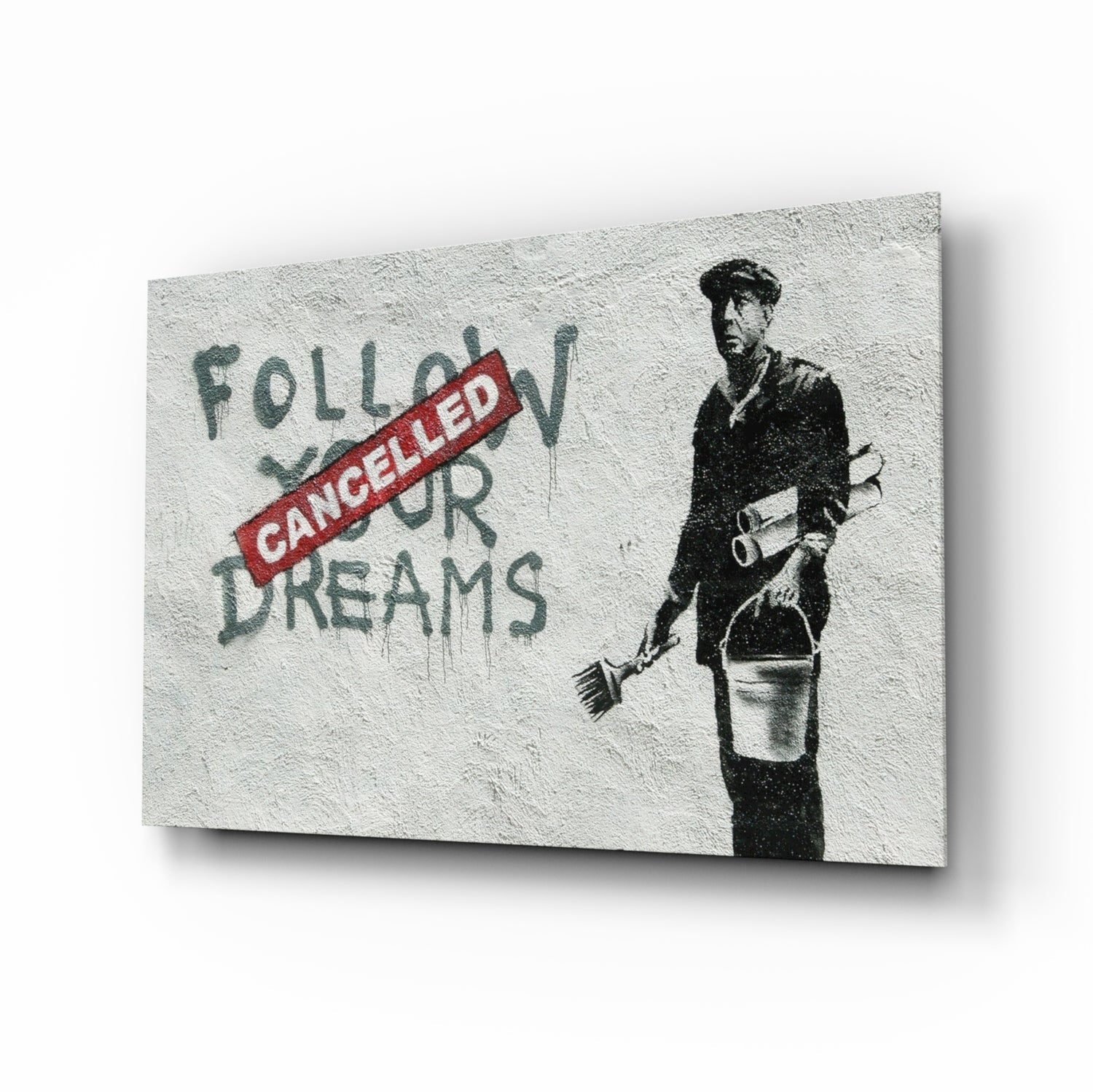 Glass art print displayed at an angle showing stenciled figure with "Follow Your Dreams" text crossed by red "Cancelled" stamp.