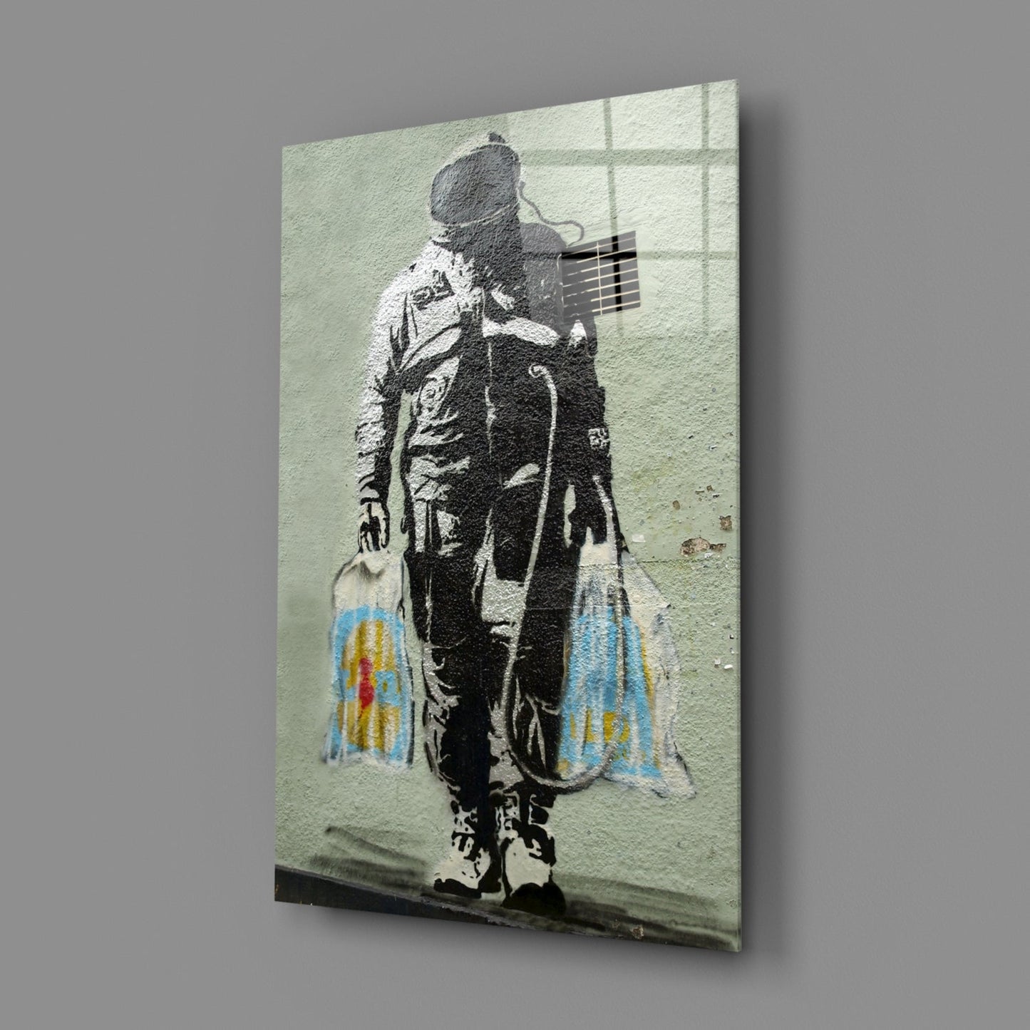 Glass art print of stenciled figure holding guitar with colorful shopping bags, mounted at angle against gray background.