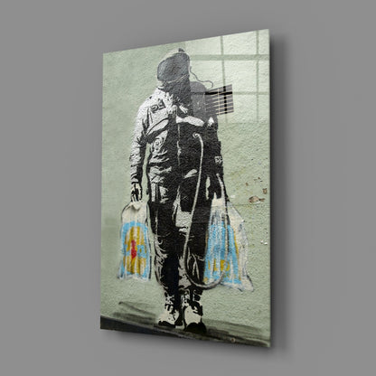 Glass art print of stenciled figure holding guitar with colorful shopping bags, mounted at angle against gray background.