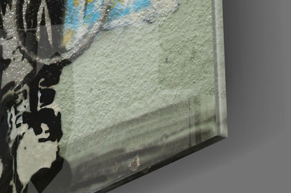 Close-up side angle of glass art panel showing textured surface with blue, yellow, and cream paint strokes and black silhouette detail.