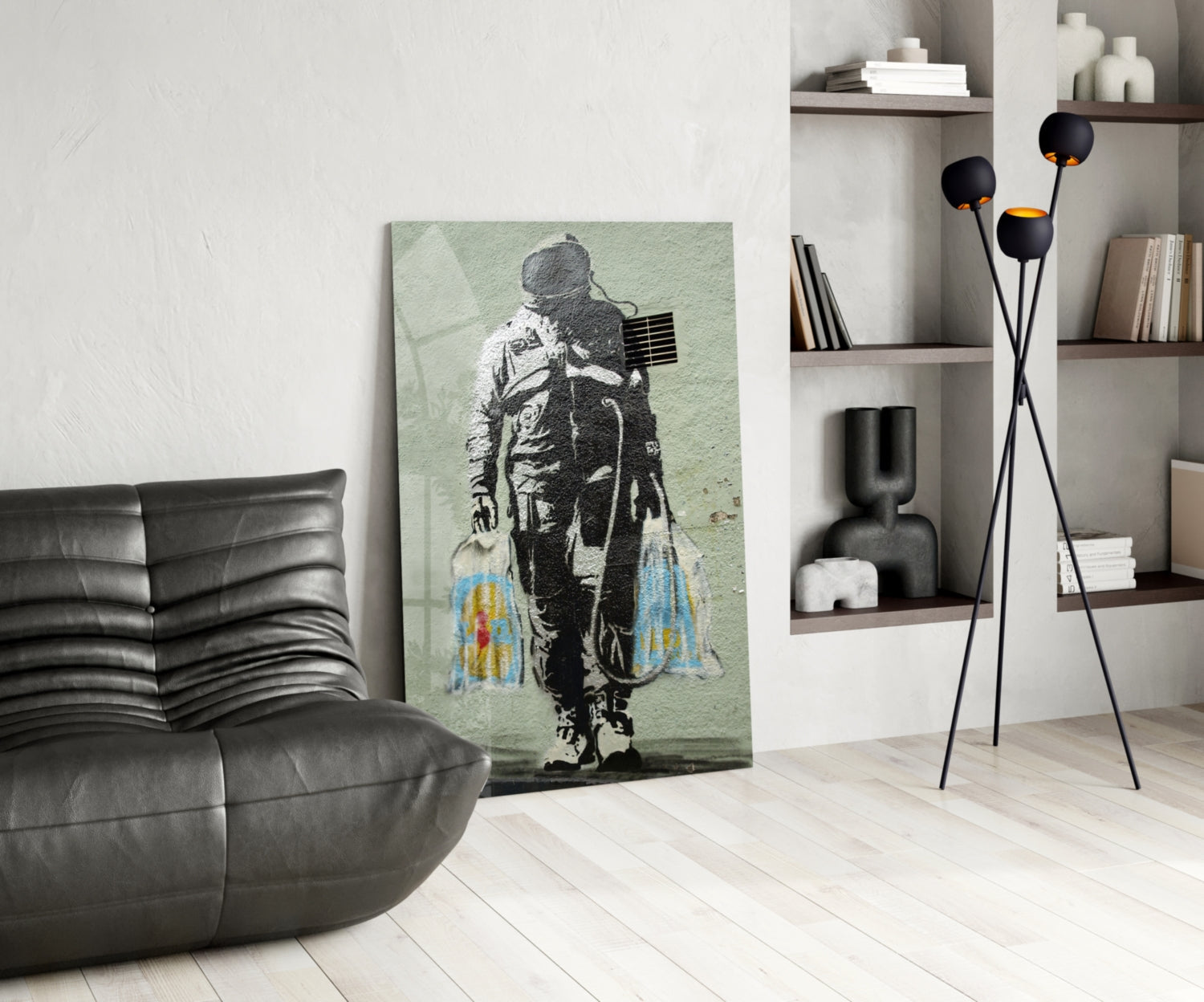 Modern living room featuring stenciled astronaut artwork on pale green glass leaning against white wall beside black leather chair.