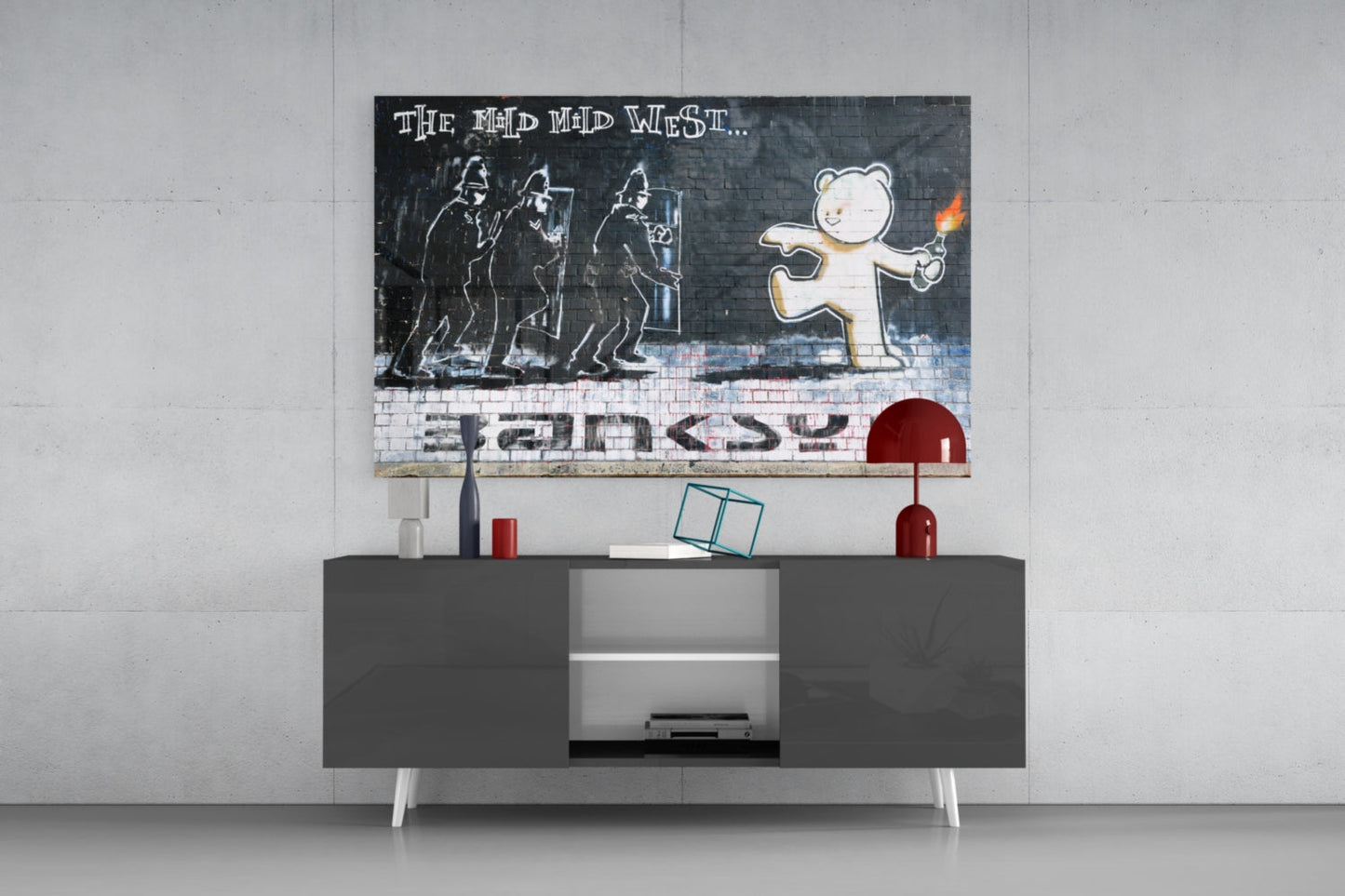 Bear's Resistance glass art mounted above gray media console displaying riot police and smiling bear with "The Mad Mad West" text and "Banksy" signature.