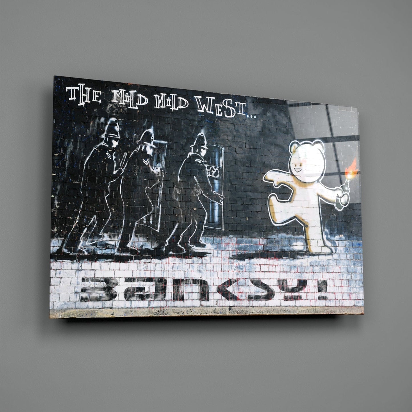 Glass art print featuring stenciled figures and teddy bear with "The Mid West... Banksy" text on brick background.