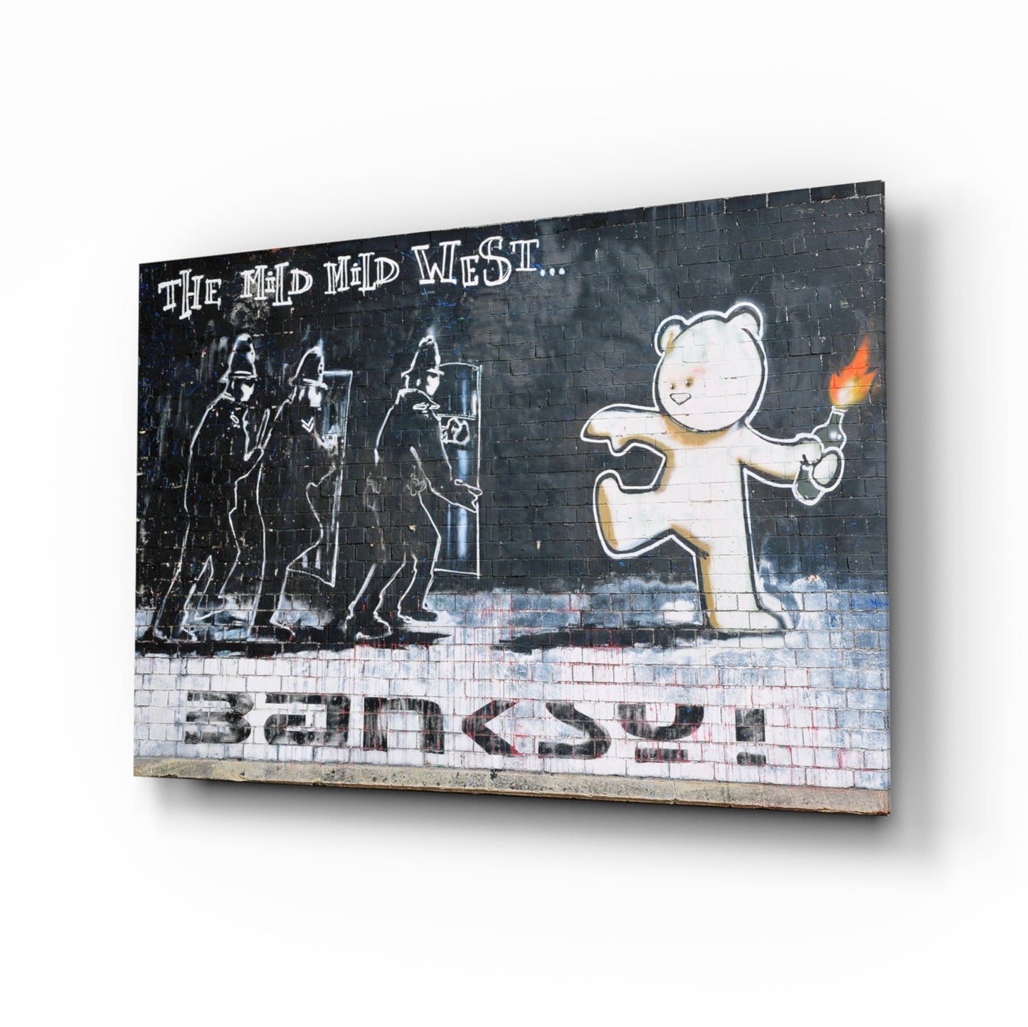 Three armed riot police face a smiling bear holding a torch against dark brick wall with "The Mad Mid West" text and "Banksy" signature.