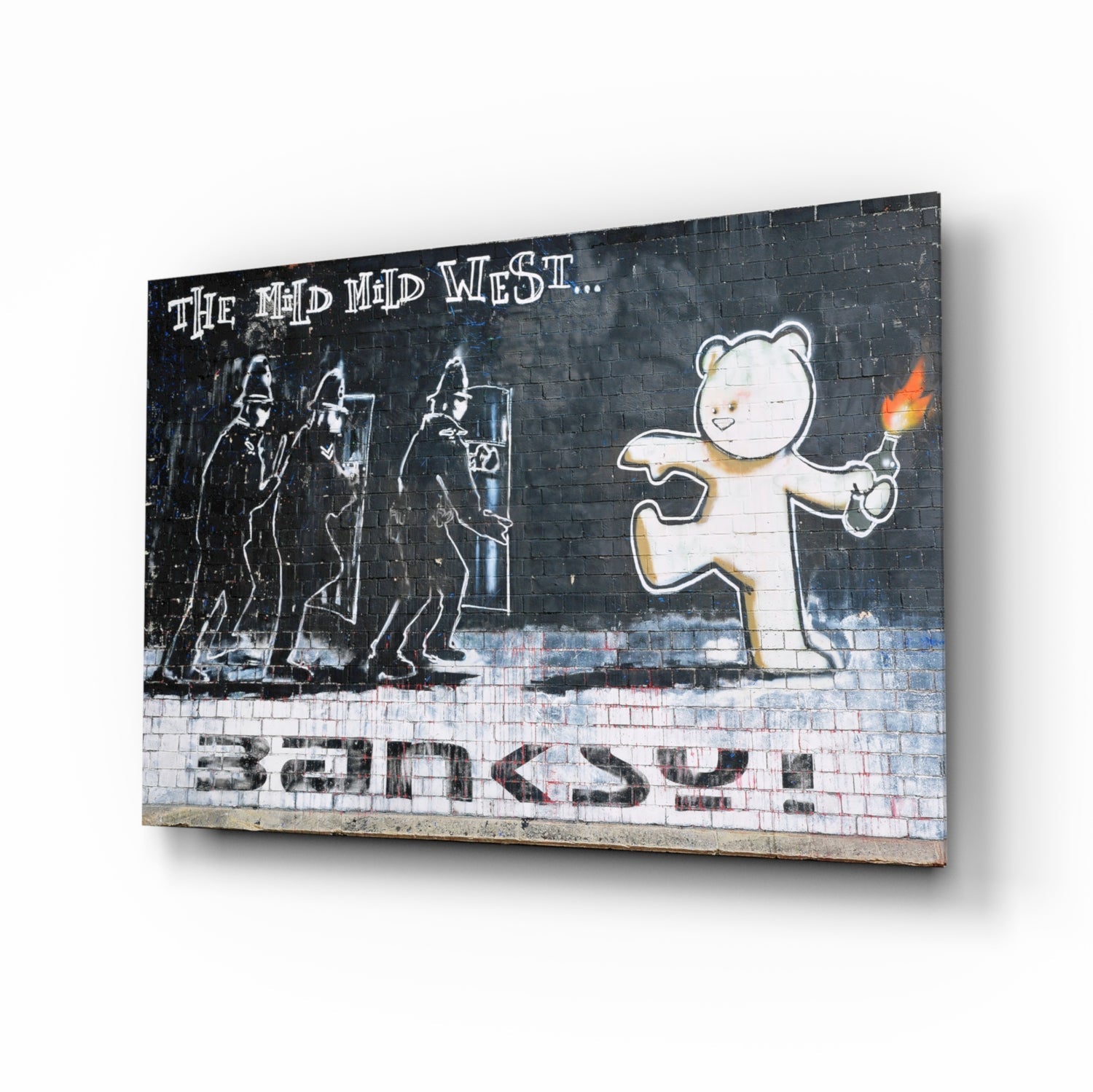 Three armed riot police face a smiling bear holding a torch against dark brick wall with "The Mad Mid West" text and "Banksy" signature.