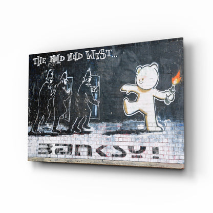 Three armed riot police face a smiling bear holding a torch against dark brick wall with "The Mad Mid West" text and "Banksy" signature.