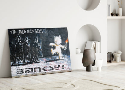 Street art glass panel leaning against white wall displays bear holding torch with police figures and "The Mid Mad West" text on brick background.