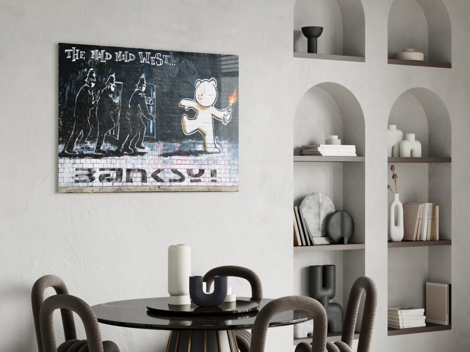 Banksy-style Bear's Resistance glass art print displayed above a round black dining table with gray chairs in a minimalist interior with built-in shelving.
