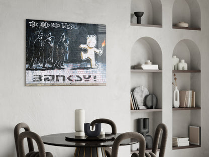 Banksy-style Bear's Resistance glass art print displayed above a round black dining table with gray chairs in a minimalist interior with built-in shelving.