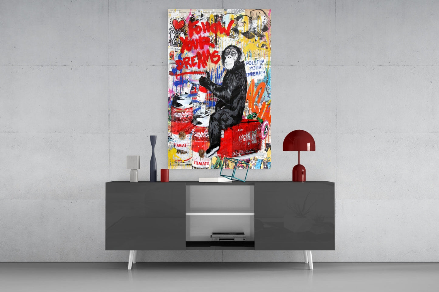 Colorful pop art glass panel featuring a black chimpanzee holding a paintbrush above a red couch, surrounded by graffiti and brand logos, displayed above a modern media console.