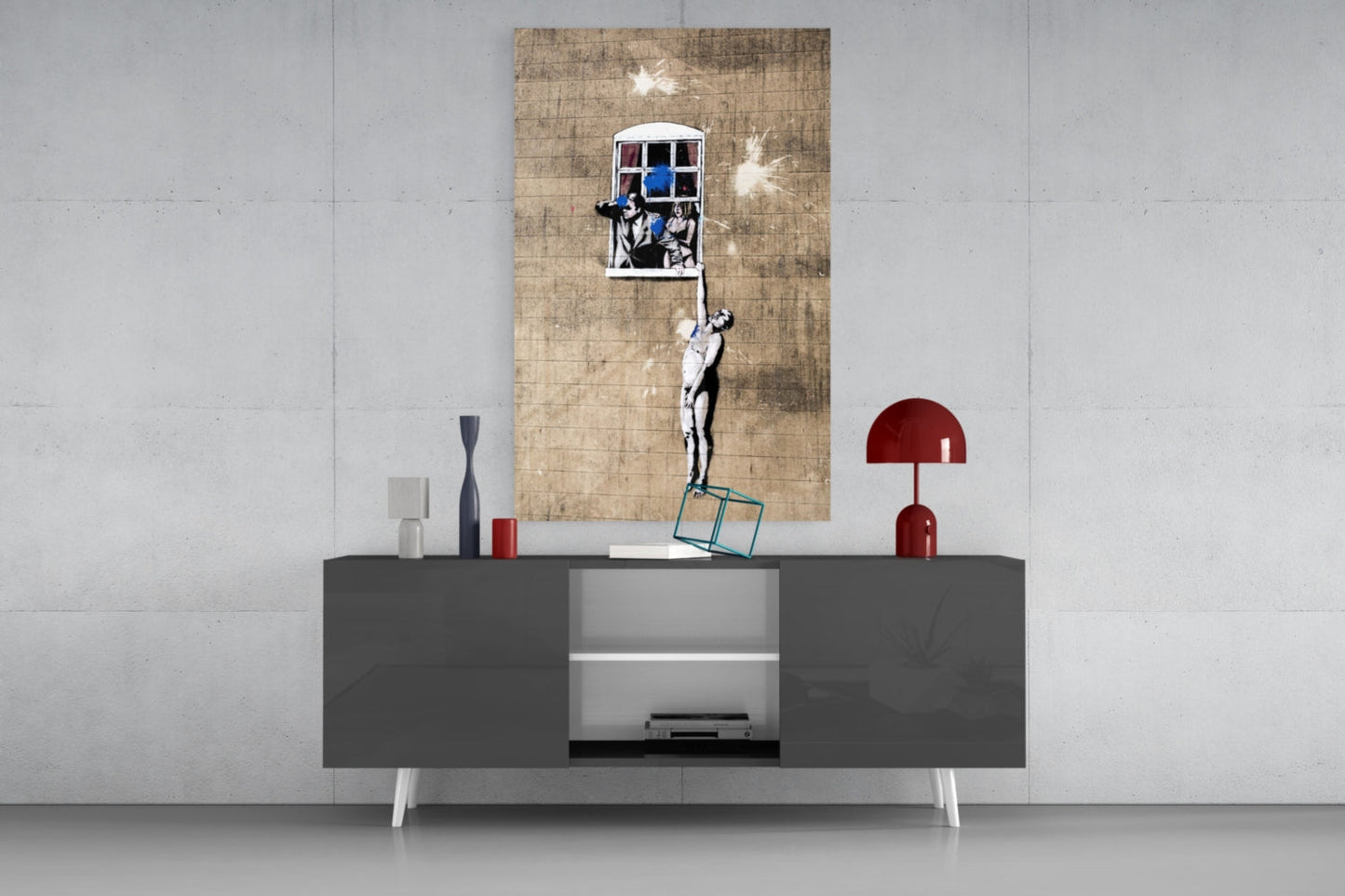 Banksy street art print displayed on tan textured canvas above dark gray media console with red lamp and decorative objects.