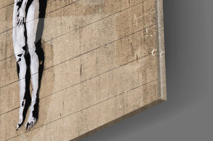 Street art stencil of white legs on tan concrete wall with horizontal lines and shadow.