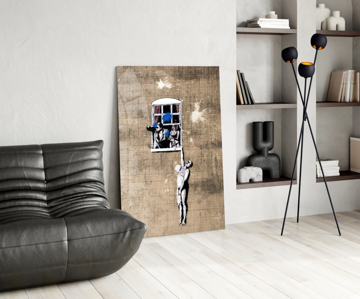 Modern living room interior featuring Banksy-style stencil art on wooden panel of figure reaching toward window with blue sky, displayed against white wall.