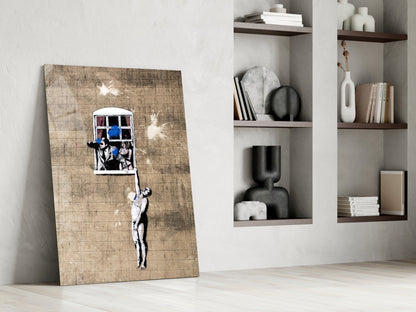 Banksy-style glass art on distressed wood leaning against white wall with floating shelves displaying decorative objects.