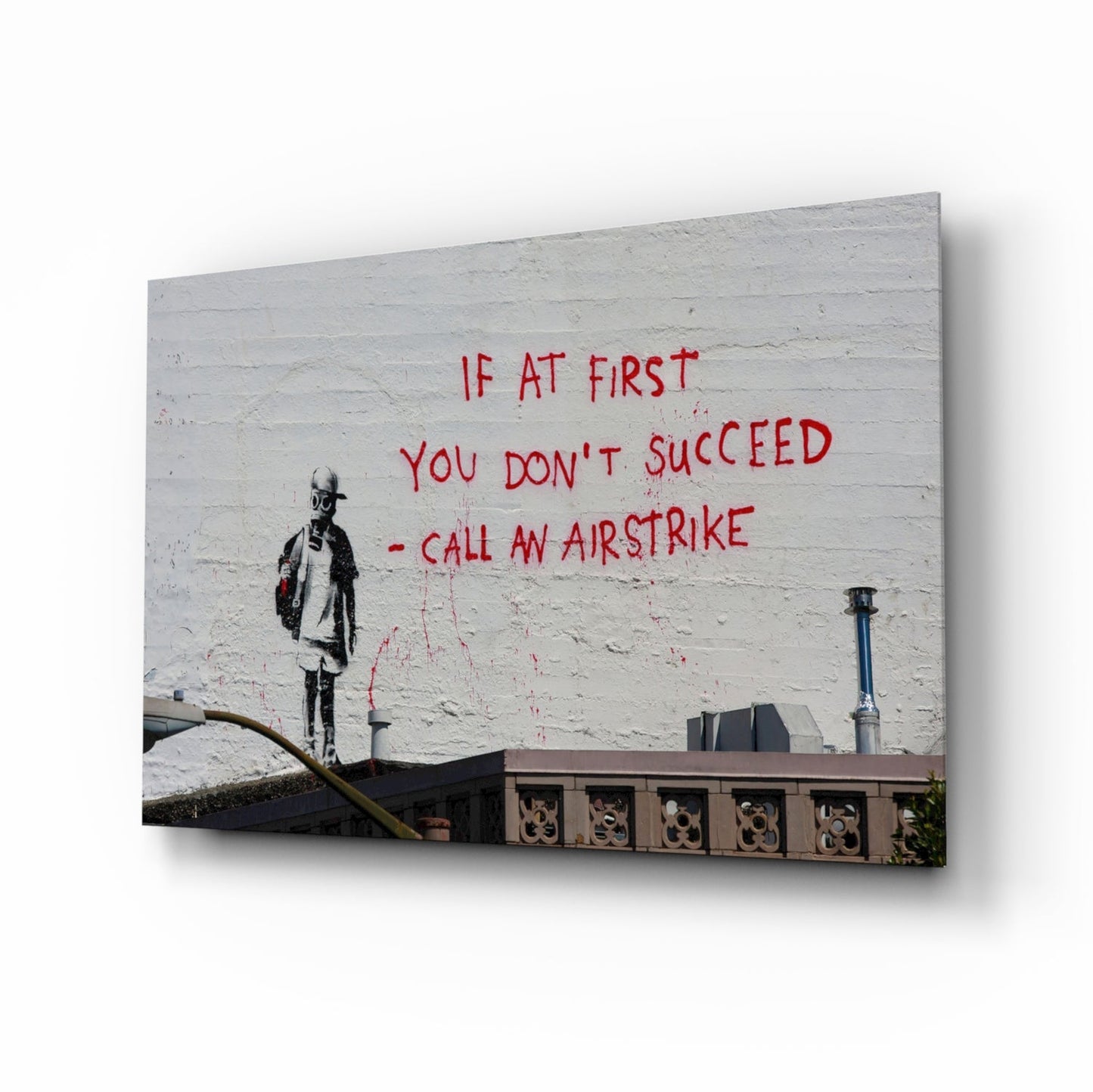 Glass art canvas displaying street art featuring a stenciled figure and red text reading "If at first you don't succeed - call an airstrike" on white brick wall.