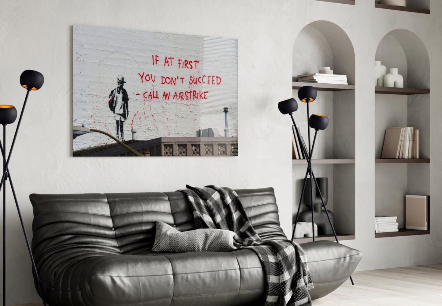 Banksy-style street art glass print displayed above black leather sofa in modern living room with white built-in shelving.