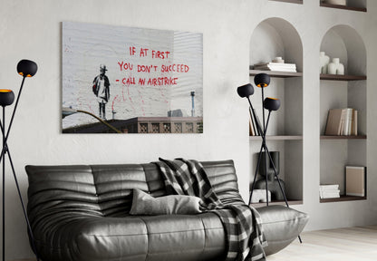 Banksy-style street art glass print displayed above black leather sofa in modern living room with white built-in shelving.