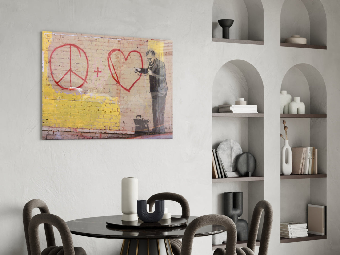 Street art glass print depicting figure with peace symbol and heart in red on weathered brick wall, displayed above black dining table in modern interior.