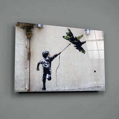 Glass art print of stenciled child figure holding string attached to green and black bird silhouette on white wall.