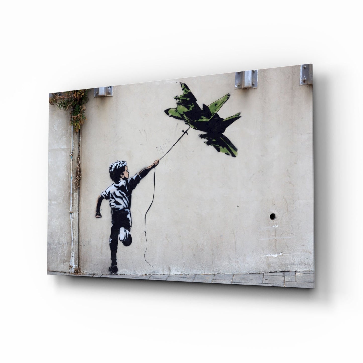 Glass print of Banksy's "Boy with Kite" street art mounted on wall, showing child reaching toward bird in black stencil style on weathered concrete background.