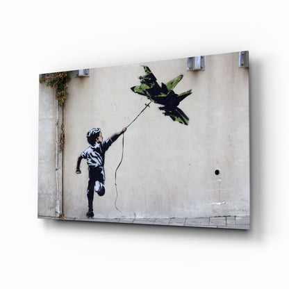 Glass print of Banksy's "Boy with Kite" street art mounted on wall, showing child reaching toward bird in black stencil style on weathered concrete background.
