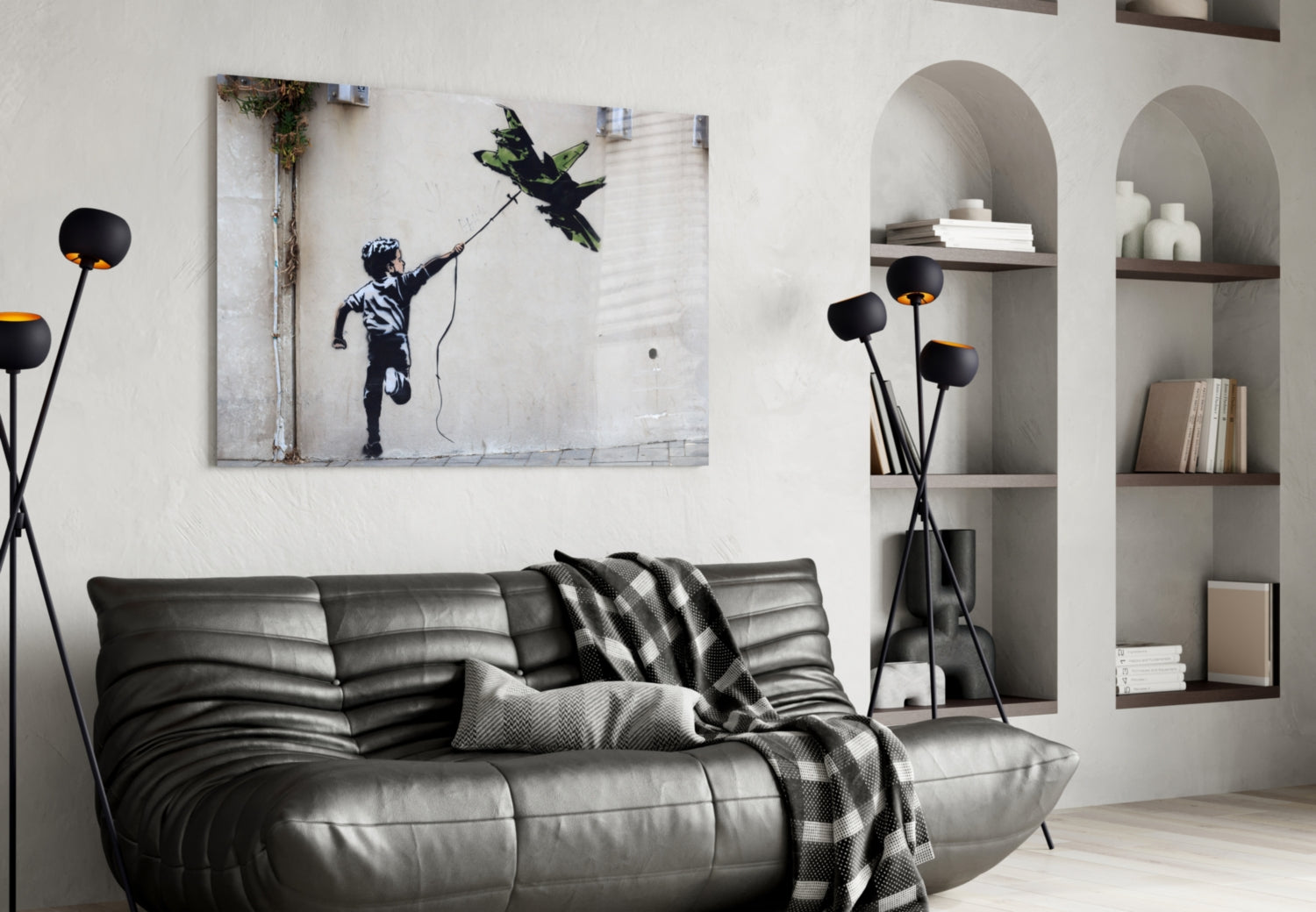Black leather sofa with patterned throw blanket beneath framed Banksy-style street art print of child reaching for kite, flanked by arched wall shelving.